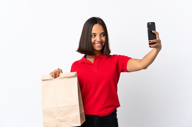 Joven mujer latina sosteniendo una bolsa de compras aislada en blanco haciendo un selfie