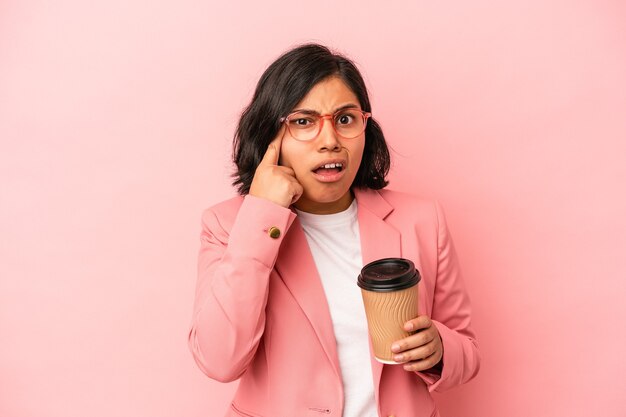 Joven mujer latina sosteniendo café para llevar aislado sobre fondo rosa mostrando un gesto de decepción con el dedo índice.