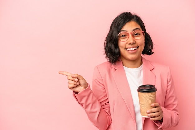 Joven mujer latina sosteniendo café para llevar aislado sobre fondo rosa sonriendo y apuntando a un lado, mostrando algo en el espacio en blanco.