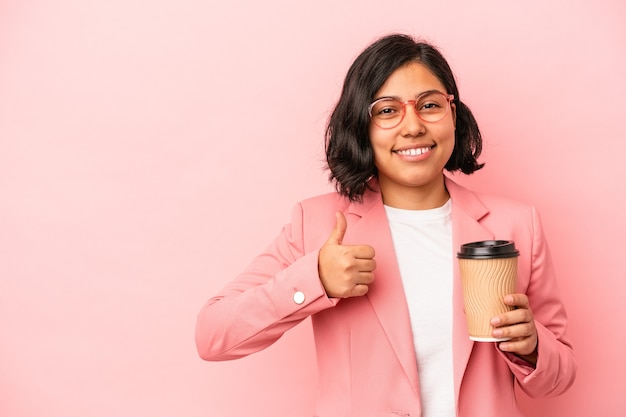 Joven mujer latina sosteniendo café para llevar aislado sobre fondo rosa sonriendo y levantando el pulgar hacia arriba