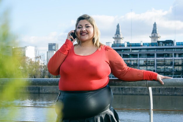 joven mujer latina de talla grande al aire libre sonriendo hablando por teléfono