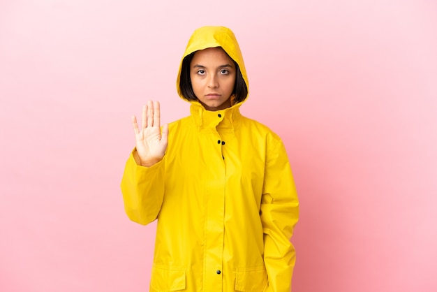 Joven mujer latina vistiendo un abrigo impermeable sobre antecedentes aislados haciendo gesto de parada