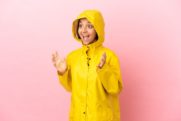 Joven mujer latina vistiendo un abrigo impermeable sobre fondo aislado con expresión facial sorpresa