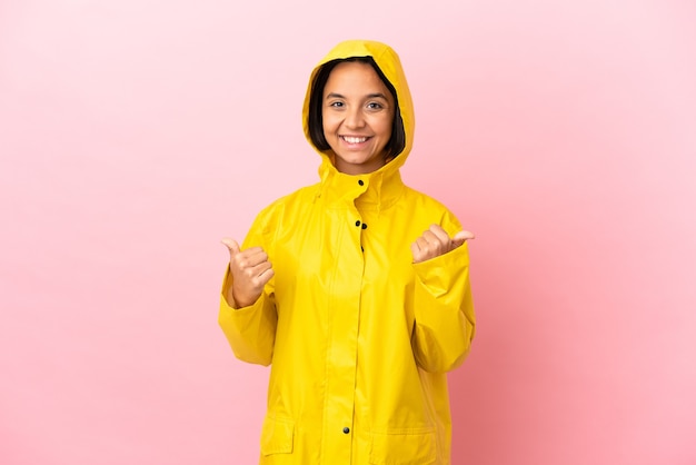 Foto joven mujer latina vistiendo un abrigo impermeable sobre fondo aislado con gesto de pulgar hacia arriba y sonriente