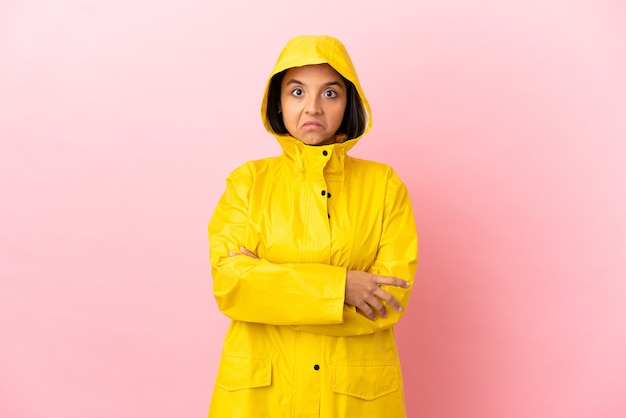 Joven mujer latina vistiendo un abrigo impermeable sobre fondo aislado haciendo gesto de dudas mientras levanta los hombros