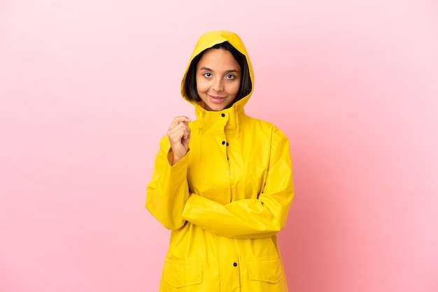 Joven mujer latina vistiendo un abrigo impermeable sobre fondo aislado riendo