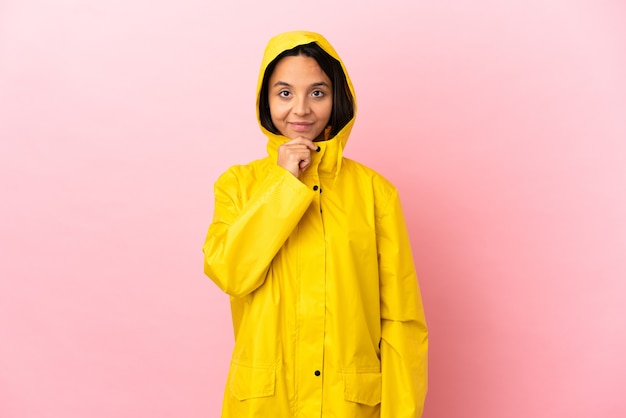 Joven mujer latina vistiendo un abrigo impermeable sobre pensamiento de fondo aislado