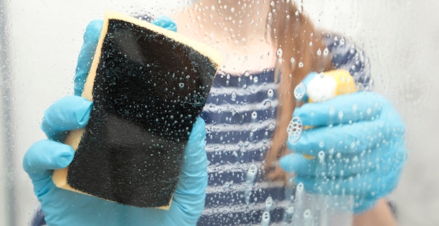 La joven mujer limpiando el cristal en la ducha