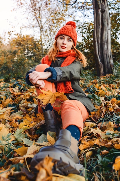 Foto joven mujer linda y brillante con sombrero y bufanda de punto cálido de color naranja sobre un fondo de hojas amarillas de otoño