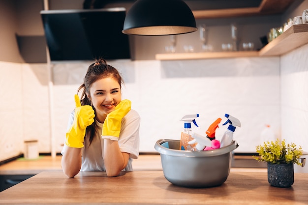 Joven mujer linda feliz en guantes amarillos está limpiando su cocina en casa con detergentes