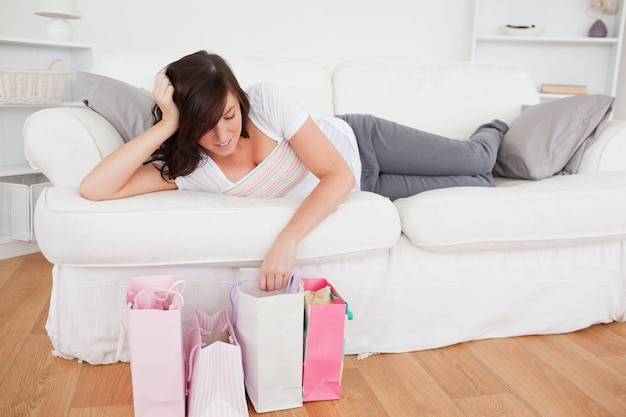 Joven mujer linda posando con sus bolsas de compras mientras está acostado en un sofá