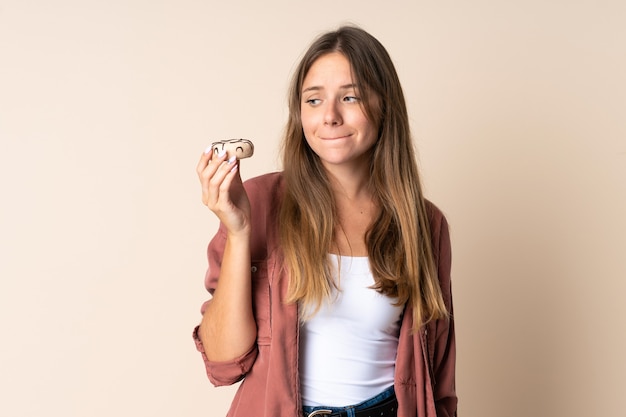 Joven mujer lituana aislada en beige sosteniendo una rosquilla