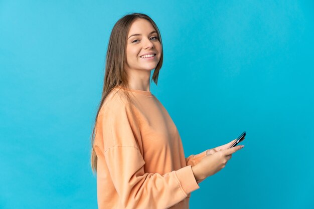 Joven mujer lituana aislada sobre fondo azul enviando un mensaje o correo electrónico con el móvil