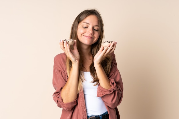 Joven mujer lituana aislada sobre fondo beige con donuts