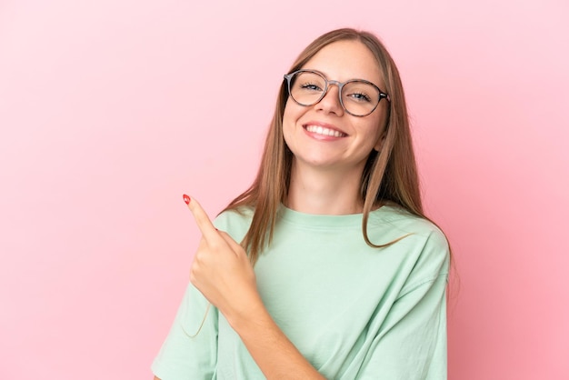 Joven mujer lituana aislada sobre fondo de color rosa con gafas y apuntando hacia el lado