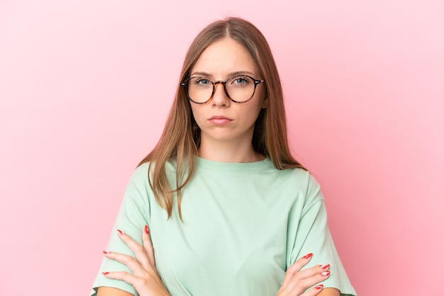 Joven mujer lituana aislada sobre fondo rosa con gafas y brazos cruzados