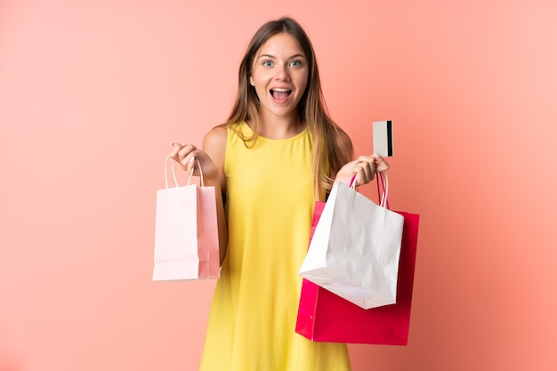 Joven mujer lituana aislada sobre fondo rosa sosteniendo bolsas de compras y sorprendido