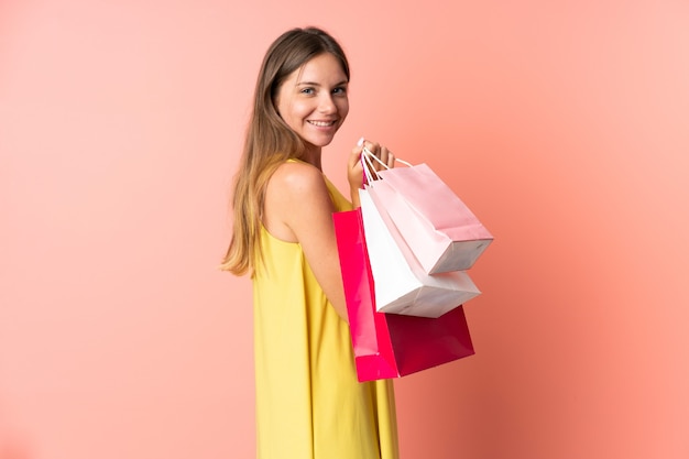 Joven mujer lituana en rosa sosteniendo bolsas de compras y sonriendo