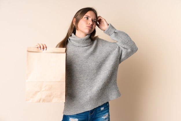 Joven mujer lituana sosteniendo una bolsa de compras con dudas y con expresión de la cara confusa