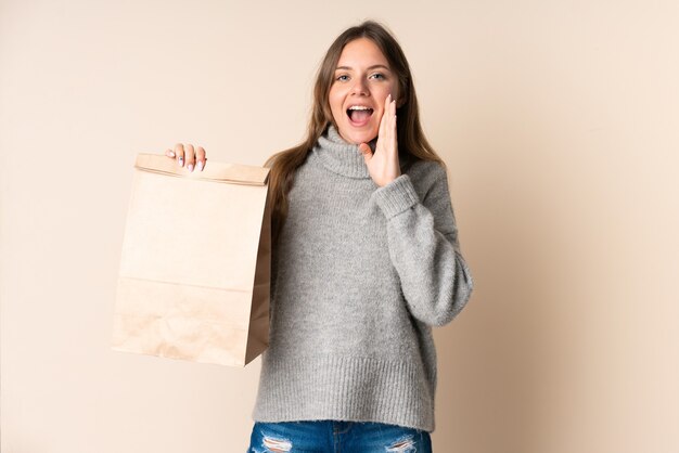 Joven mujer lituana sosteniendo una bolsa de compras gritando con la boca abierta