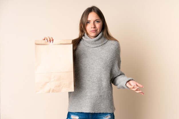 Joven mujer lituana sosteniendo una bolsa de compras haciendo gesto de dudas mientras levanta los hombros