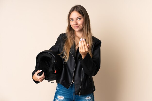 Joven mujer lituana sosteniendo un casco de moto aislado en beige invitando a venir con la mano. Feliz de que hayas venido