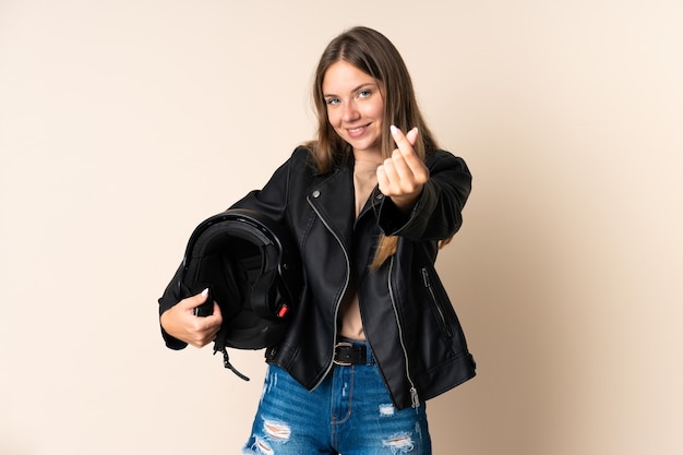 Joven mujer lituana sosteniendo un casco de motocicleta aislado en pared beige haciendo gesto de dinero