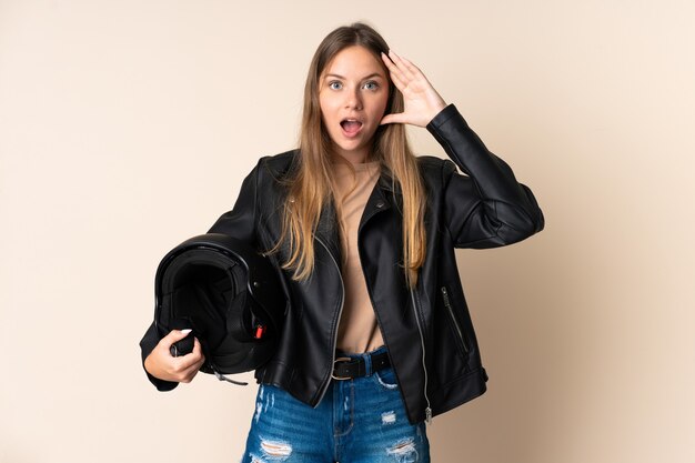 Joven mujer lituana sosteniendo un casco de motocicleta aislado sobre fondo beige con expresión de sorpresa