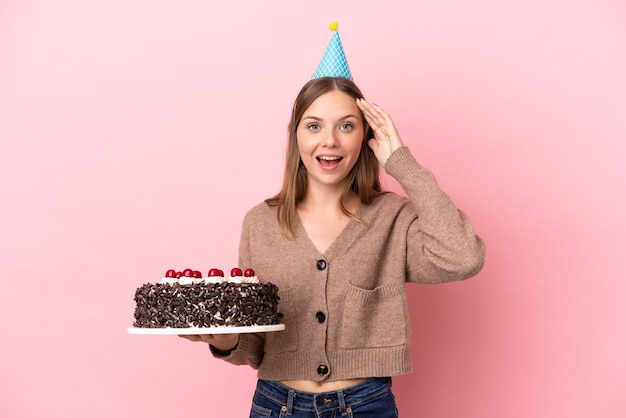 Joven mujer lituana sosteniendo pastel de cumpleaños aislado sobre fondo rosa con expresión de sorpresa