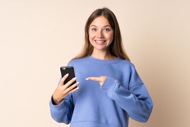 Foto joven mujer lituana con teléfono móvil en beige con expresión facial sorpresa