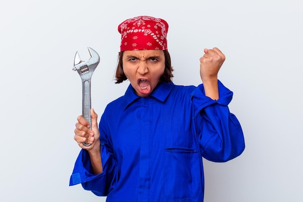 Joven mujer mecánica sosteniendo una llave aislada levantando el puño después de una victoria, concepto ganador.