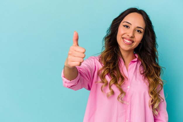 Joven mujer mexicana aislada en la pared azul sonriendo y levantando el pulgar hacia arriba