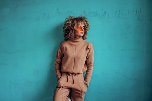 Foto joven mujer de moda sonriente con el pelo rizado apoyado contra la pared.