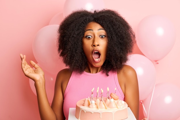 Una joven mujer moderna celebrando un cumpleaños lista para soplar las velas  en un pastel rosa con globos rosas aislados | Foto Premium