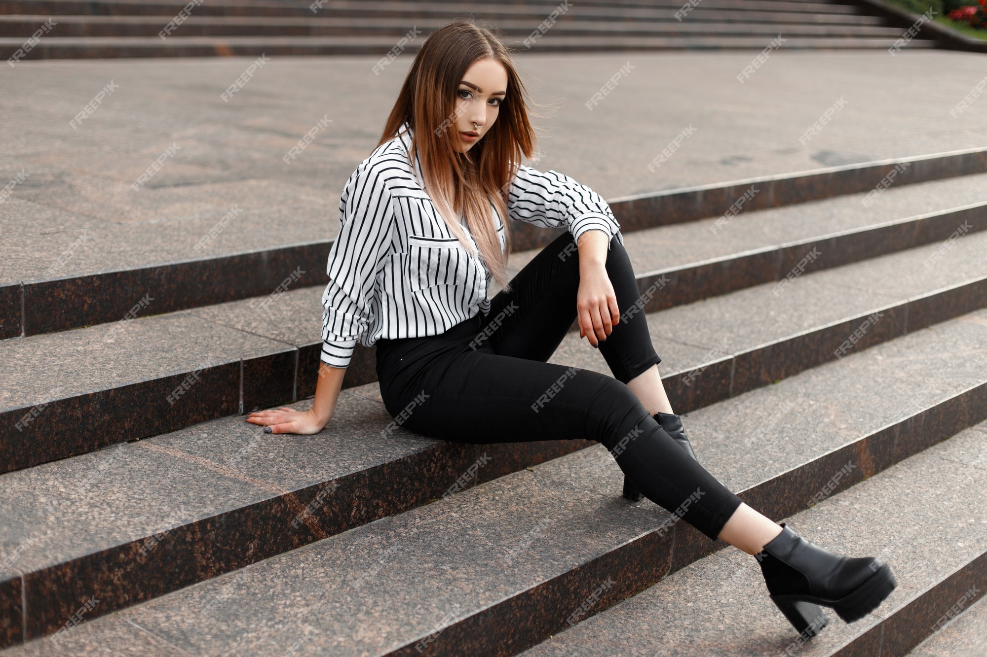 Joven mujer moderna en jeans de moda en una camisa a rayas de moda en zapatos de cuero negro en una escalera vintage en la ciudad en un cálido día de