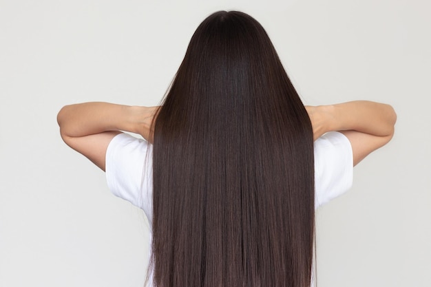 Joven mujer morena con una camiseta blanca mostrando su hermoso cabello largo, liso y saludable.
