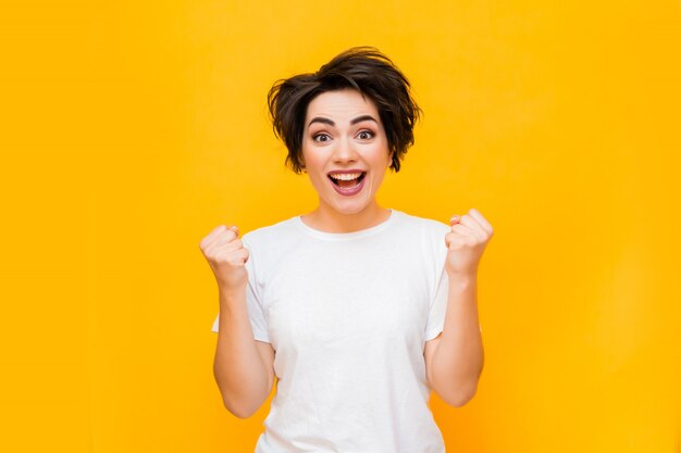 Joven mujer morena feliz con un corte de pelo corto en una camiseta blanca sobre un fondo amarillo. retrato de una mujer joven con diversas emociones sobre un fondo amarillo. espacio para texto