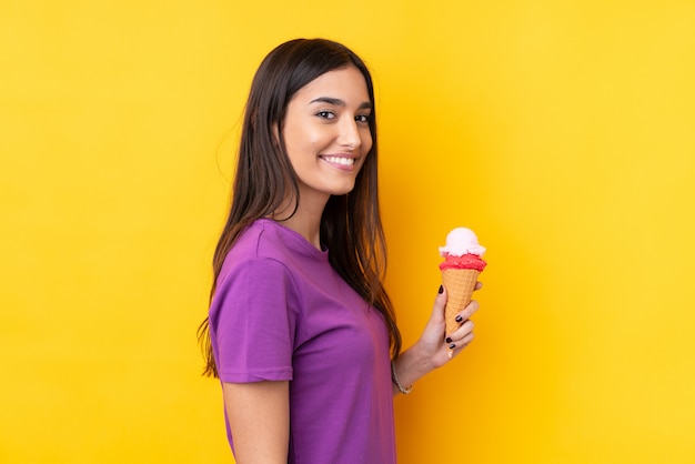 Joven mujer morena con un helado de cucurucho sobre pared amarilla aislada sonriendo mucho