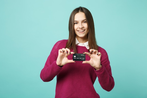 Joven mujer morena con ropa informal posando aislada en un retrato de estudio de fondo azul turquesa. Gente emociones sinceras concepto de estilo de vida. Simulacros de espacio de copia. Mantenga en la mano la tarjeta bancaria de crédito.