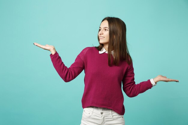 Joven mujer morena con ropa informal posando aislada en un retrato de estudio de fondo de pared turquesa verde azul. Gente emociones sinceras concepto de estilo de vida. Simulacros de espacio de copia. extendiendo las manos.