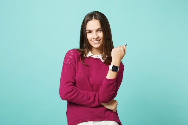 Joven mujer morena con ropa informal posando aislada en un retrato de estudio de fondo de pared turquesa verde azul. Gente emociones sinceras concepto de estilo de vida. Simulacros de espacio de copia. reloj inteligente a mano.