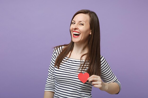 Joven mujer morena con ropa informal a rayas posando aislada en un retrato de estudio de fondo morado violeta. Concepto de estilo de vida de emociones sinceras de personas Espacio de copia simulado Mantenga dos pequeños corazones rojos