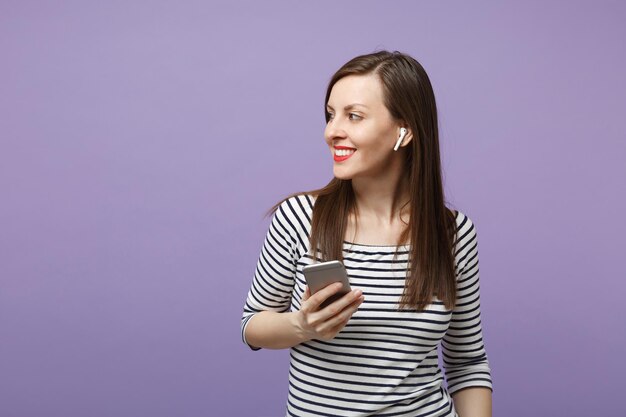 Joven mujer morena con ropa informal a rayas posando aislada en un retrato de estudio de fondo morado violeta. Gente emociones sinceras concepto de estilo de vida. Simulacros de espacio de copia. Mantenga la conversación del teléfono móvil.