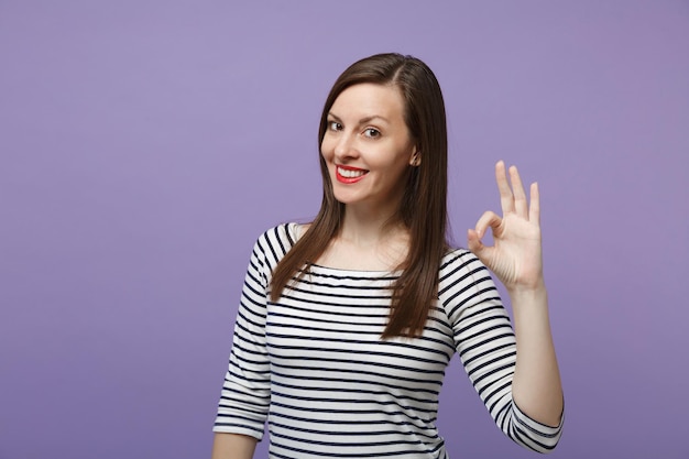 Joven mujer morena con ropa informal a rayas posando aislada en un retrato de estudio de fondo morado violeta. Gente emociones sinceras concepto de estilo de vida. Simulacros de espacio de copia. Mostrando un gesto bien bien.