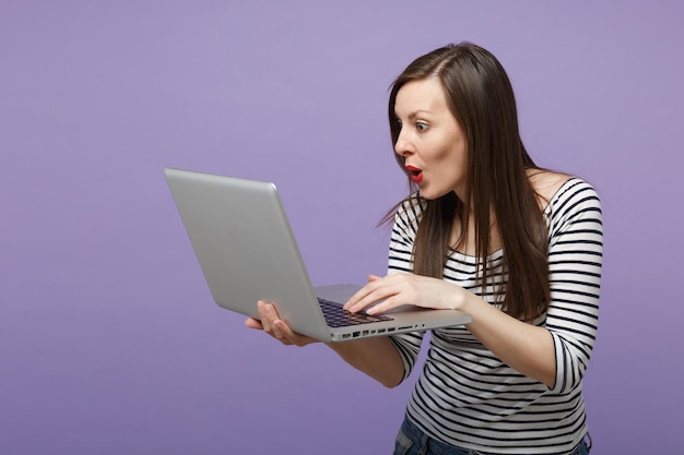 Joven mujer morena con ropa informal a rayas posando aislada en un retrato de estudio de fondo morado violeta. Gente emociones sinceras concepto de estilo de vida. Simulacros de espacio de copia. Sostenga la computadora de la tableta.