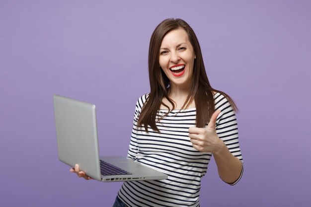 Joven mujer morena con ropa informal a rayas posando aislada en un retrato de estudio de fondo morado violeta. Gente emociones sinceras concepto de estilo de vida. Simulacros de espacio de copia. Sostenga la computadora de la tableta.