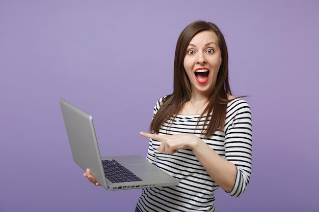 Joven mujer morena con ropa informal a rayas posando aislada en un retrato de estudio de fondo morado violeta. Gente emociones sinceras concepto de estilo de vida. Simulacros de espacio de copia. Sostenga la computadora de la tableta.