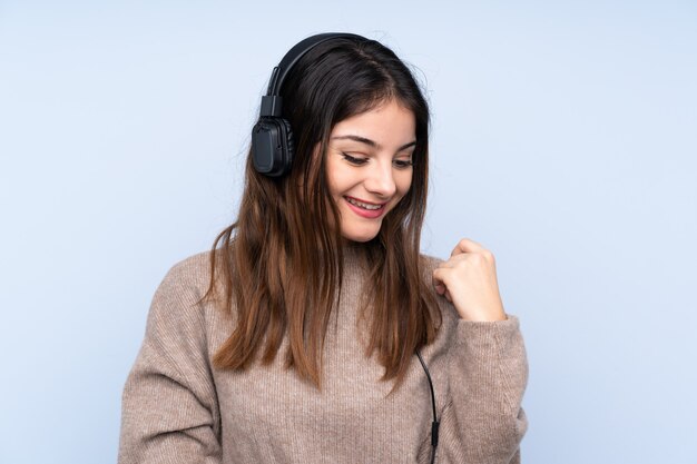 Joven mujer morena sobre pared azul escuchando música