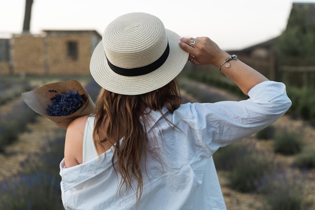 Foto joven mujer morena con sombrero de paja mira a la distancia contra el fondo de una joven lavanda en flor retrato en primer plano de una hermosa chica sosteniendo un ramo de flores en las manos textura agrícola