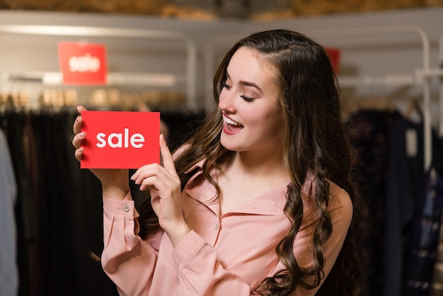 Joven mujer morena sonriente tiene carteles rojos con palabra de venta